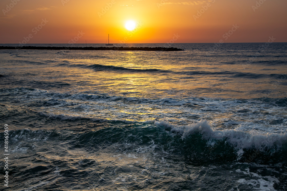 Sailing boat at sunset in orange tones over the Mediterranean sea in Tel Aviv, Israel