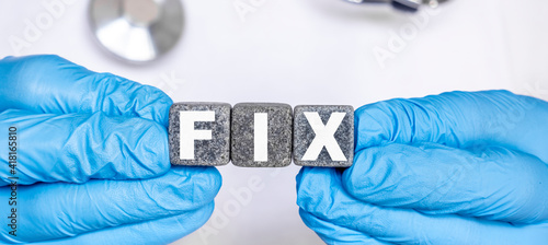 FIX - word from stone blocks with letters holding by a doctor's hands in medical protective gloves
