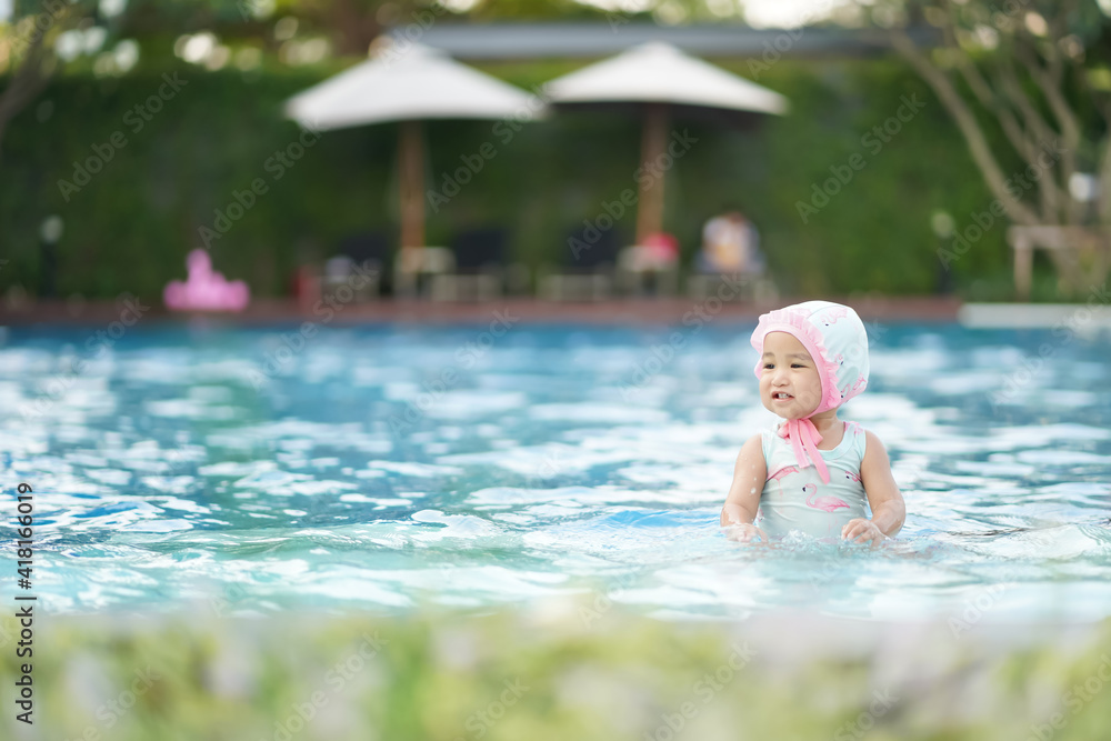 Asian cute baby girl in swimsuit enjoying in the swimming pool with copy space