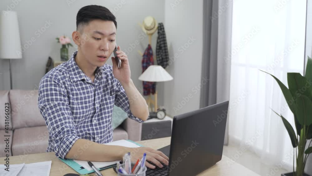 asian businessman working on the computer is celebrating with striking gesture after receiving good business news on the phone at home. asian businessman working on the computer is celebrating with striking gesture after receiving good business news on the phone at home.