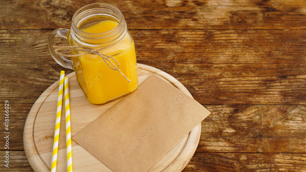 Fototapeta premium Orange juice in a glass jar on a wooden background. Envelope with a letter