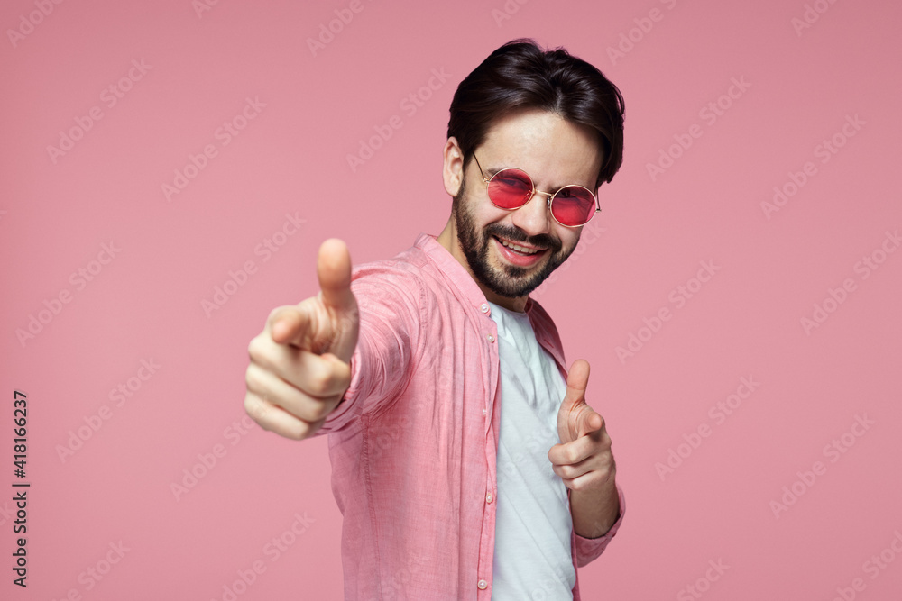 Handsome man in pink shirt and sunglasses showing pointing gesture on pink background. Handsome man in pink shirt and sunglasses showing pointing gesture on pink background.