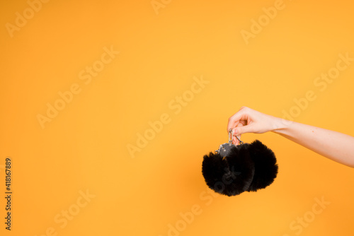 Close-up of a female hand with black handcuffs from a sex shop for adult games on an orange background. Space for text