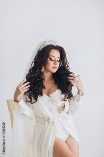 Bride.Young fashion model with perfect skin and makeup, white background. Beautiful bride on background white stairs. A woman in a long white dress is sitting on the stairs.
