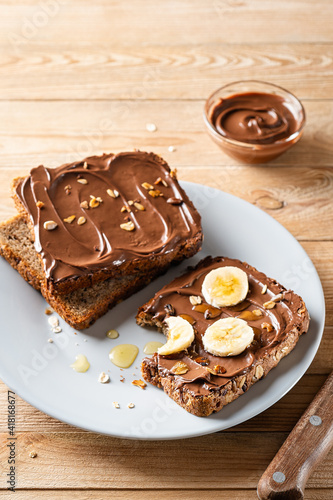 Fresh toasts with chocolate spread, slices of banana and honey on a gray plate