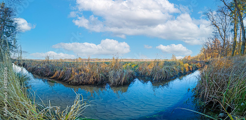 Panoramic image of natural stream in front of large meadow area in sunshine