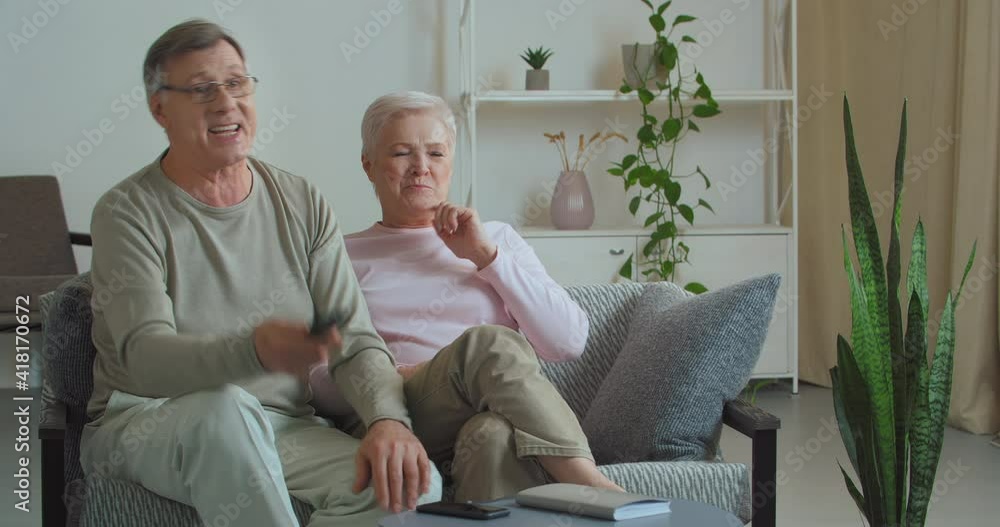 Couple of old caucasian people watching TV together cheering for their favorite sports team in championship football competition emotionally react to loss shouting words of support loudly at home