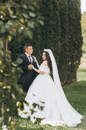 Portrait of happy newly wife and husband hugging outdoors and smiling, with waving veil and wedding bouquet made of white peonies. Sincere feelings of two young people. Concept of true immortal love.