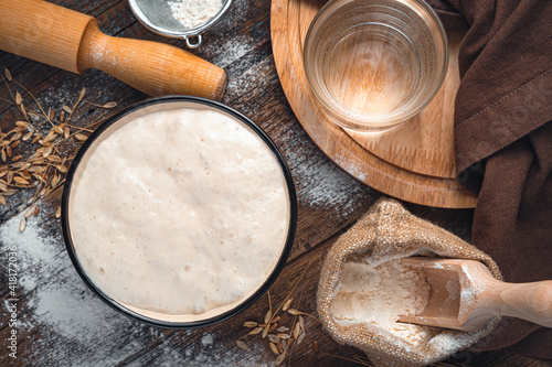 Ingredients for making bread. Active starter culture, flour, water on a brown wooden background.