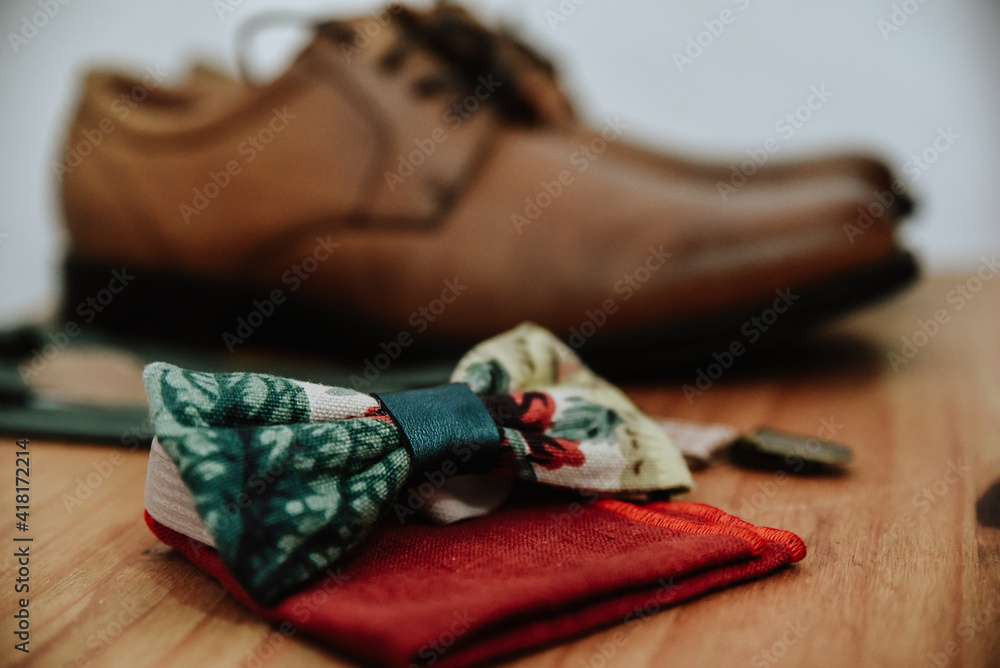 Closeup shot of a colorful bow tie on a red handkerchief with brown shoes in the background - obrazy, fototapety, plakaty 