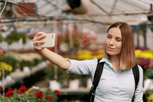 Young beautiful ladie making selfie on flowers background in the greenhouse photo