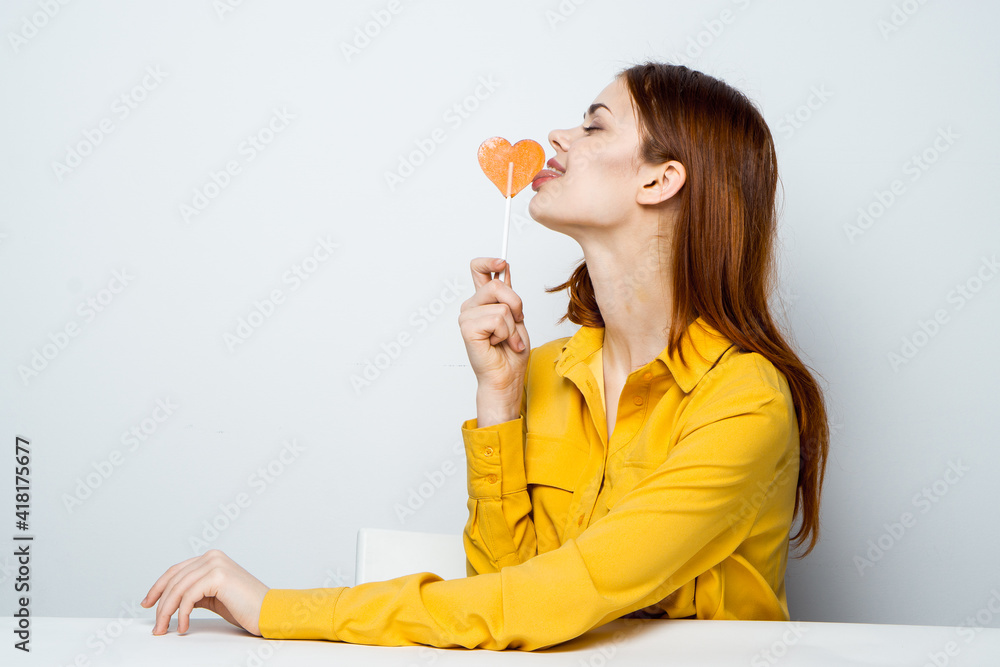pretty woman with lollipop like in a yellow shirt sits at the table emotions pretty woman with lollipop like in a yellow shirt sits at the table emotions