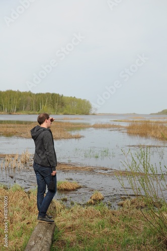 A young man stands on the shore of a reservoir and looks into the distance. Comfortable sportswear for every day. Overgrown lake.  © Ольга Толкачева