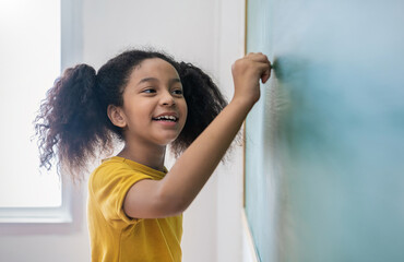 Closeup portrait of young happy African little girl write on chalk board. student writing on blackboard wall. Idea creative education knowledge back to school concept
