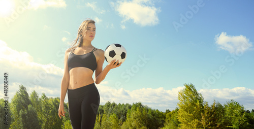 Young sports woman in black with a soccer ball in her hands on a background of the forest and blue sky
