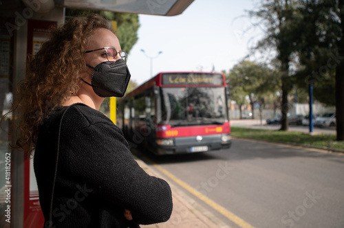 Young woman with black mask waiting for the bus in the city. Covid 19 prevention
