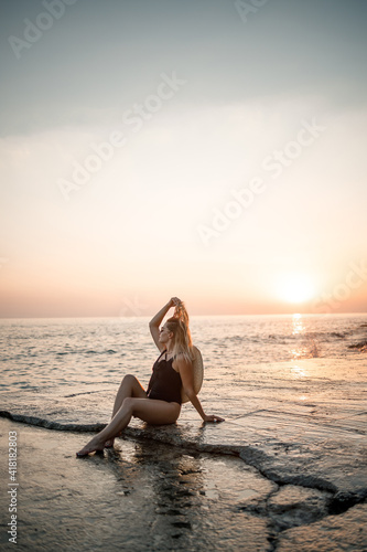 Young woman in sunglasses is resting at the sea slender in a black swimsuit. Selective focus