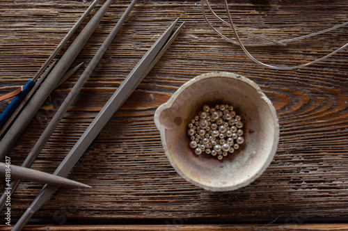 Melting pot with silver metal granules on wooden table with jeweler tools, jewelry making workshop photo