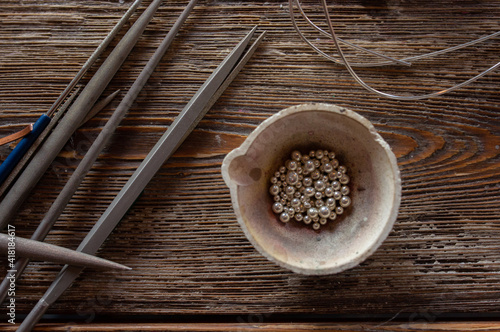 Photography Melting pot with silver metal granules on wooden table with jeweler tools, jewel