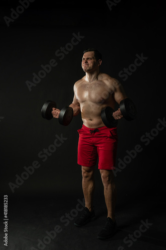 Fitness man presses dumbbells in red panties business man, attractive isolated bodybuilder. Handsome studio, fashionable elegance background black bodybuilder