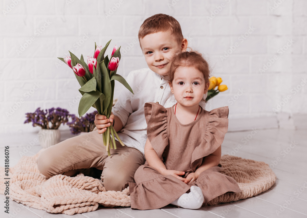 Naklejka premium Boy and girl, brother and sister sit in a white room with flowers