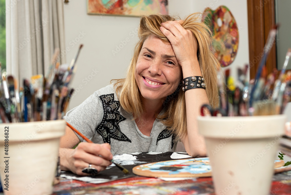Fototapeta premium young latin woman plastic artist painter very happy in her art studio with her canvases and brushes