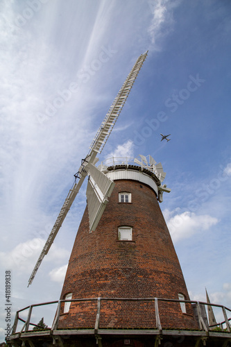 an old windmill in the country with a modern plane overhead