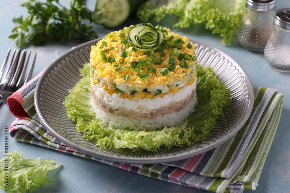 Festive salad with cod liver, rice, eggs, corn and cucumber on a plate on light blue background. Festive salad with cod liver, rice, eggs, corn and cucumber on a plate on light blue background.