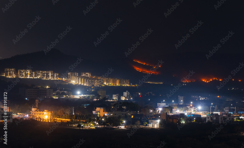 Night view of the city, controlled brush fire in the hills at the backdrop.