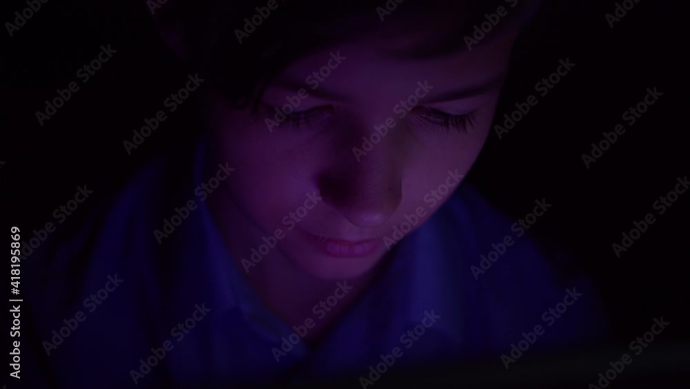 Portrait of a funny boy looking at tablet at night, Thoughtfully doing some action at night on the tablet Portrait of a funny boy looking at tablet at night, Thoughtfully doing some action at night on the tablet