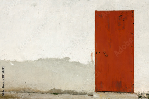 A red metal door in the plastered wall of a stone house. © kpn1968