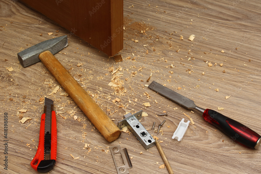 Shavings on floor from door latch installing. Wood sawdust from hole for door lock making. Hammer, chisel, knife, screws, pencil and latch by the door.