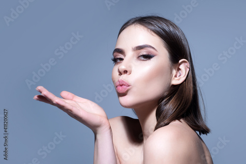 Woman with makeup blow air kiss. Goodbye on distance, isolated on grey background. photo