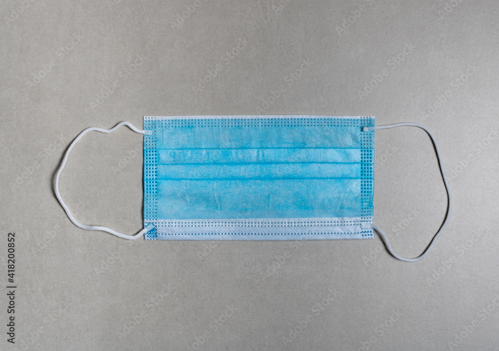 mask for personal use in combating the pandemic of the covid-19 light blue with white elastic on a gray background. mask for personal use in combating the pandemic of the covid-19 light blue with white elastic on a gray background.