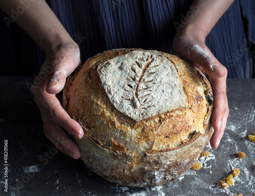 Woman in blue dress holds fresh homemade bread. Hands holding beautifully scored sourdough bread close up photo. 