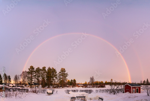 Colorful Scenic Winter Rainbow over winter snowy landscape, full size, double arch, second one not so strong. Pink frosty sky before Sunset, pine trees, much snow. Small village at background photo