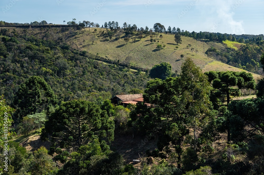 CUNHA, SAO PAULO / BRAZIL - AUG 16, 2019: View from Casa da Serra restaurant of a neighbor ranch with a building between the green vegetation and over one of the hills of Cunha mountainous landscape. CUNHA, SAO PAULO / BRAZIL - AUG 16, 2019: View from Casa da Serra restaurant of a neighbor ranch with a building between the green vegetation and over one of the hills of Cunha mountainous landscape.