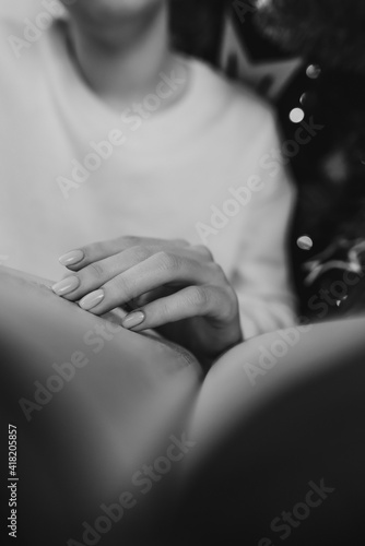 Woman in white reading interesting paper book while sitting near Christmas tree with bokeh at home. Black and white. Cozy winter pic of lady relaxing alone with novel. High quality photo