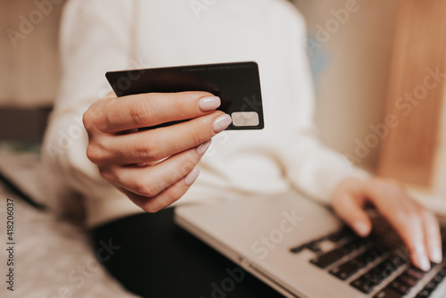 Unrecognizable woman holding credit card and using laptop computer while online shopping. Businesswoman working from home. Internet banking, money transfers concept.