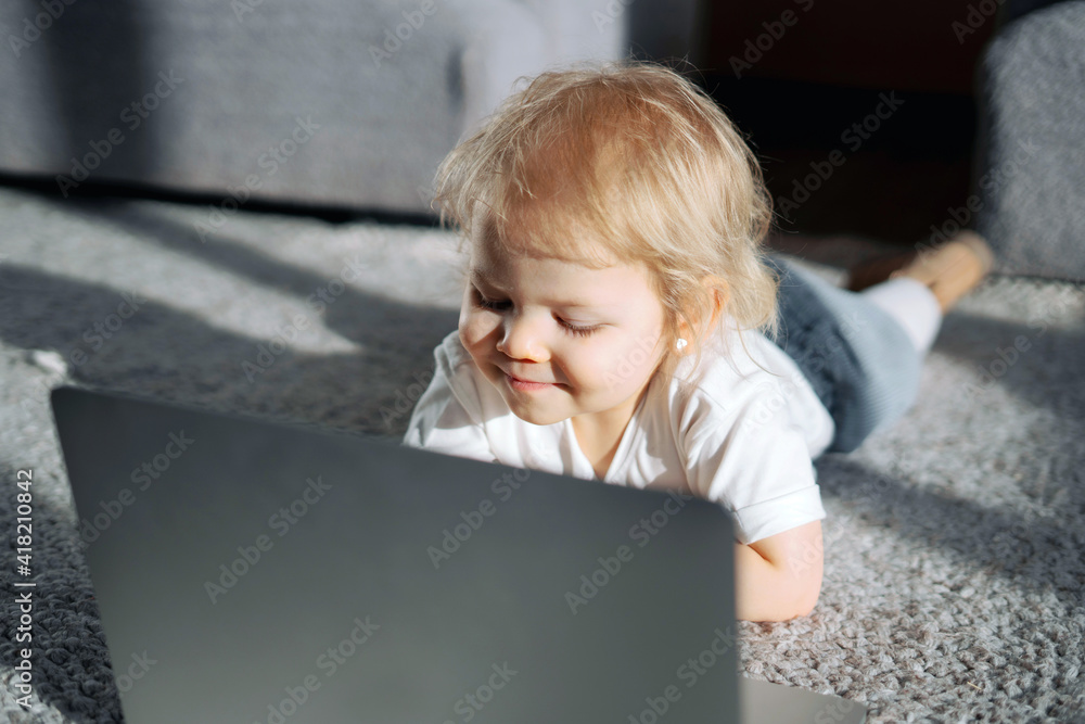 Little baby girl blonde with blue eyes. Happy childhood and youth. Favorite children's TV show cartoons. The girl's daughter looks at the laptop monitor. posing in a photo studio smiling. Little baby girl blonde with blue eyes. Happy childhood and youth. Favorite children's TV show cartoons. The girl's daughter looks at the laptop monitor. posing in a photo studio smiling.