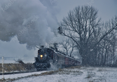 View of An Antique Restored Steam Locomotive Blowing Smoke and Steam Traveling Thru Farmlands and Countryside in a Snow Storm