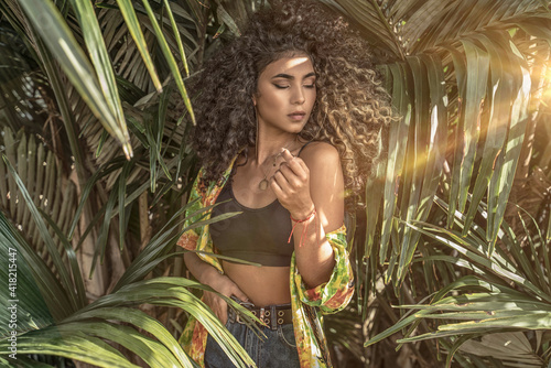 Portrait of natural beautiful afro woman posing over green palm's leafs.. photo