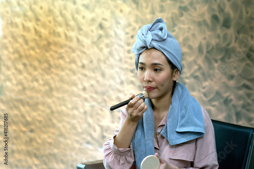 A beautiful Asian woman make up her face. With a makeup brush in hand.. © topten22photo