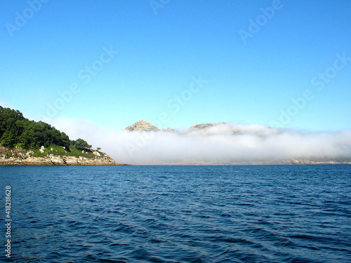 A bank of morning fog floating over water  Islac Cies  Cies Islands  Galicia  Spain  Europe  long view from an island towards the mainland  peaks of mountains visible above the cloud.