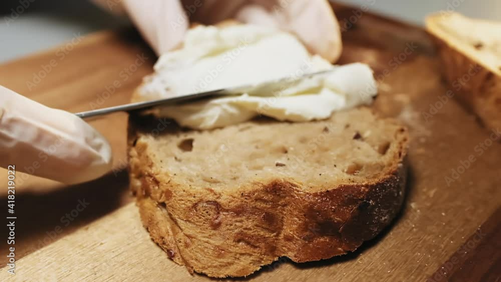 Person spreads tasty cream cheese on rye bread slice with butter knife on wooden table in kitchen extreme closeup slow motion Person spreads tasty cream cheese on rye bread slice with butter knife on wooden table in kitchen extreme closeup slow motion