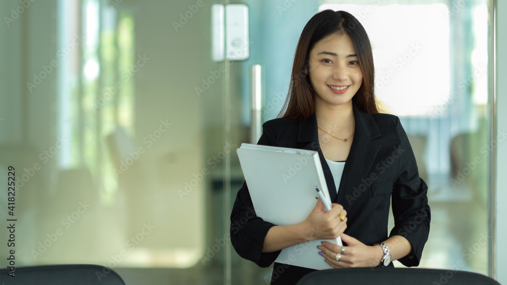 Businesswoman holding document file and smiling to camera while standing in office room