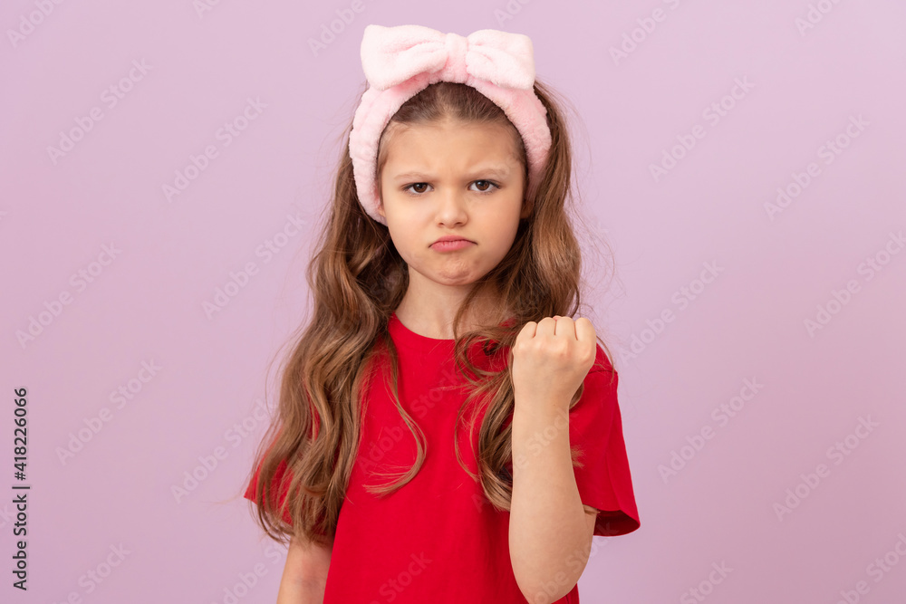 Angry little girl on pink background shows her fist. Angry little girl on pink background shows her fist.