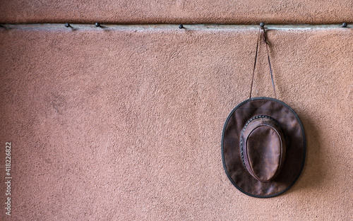 Single leather cowboy hat hanging on a row of steel pegs on an adobe wall