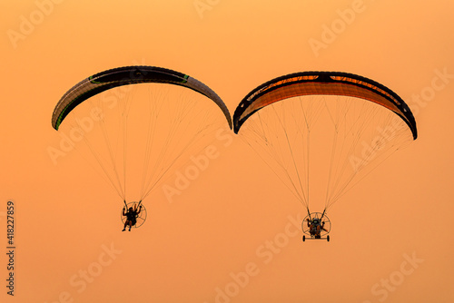 Silhouette of the Paramotor gliding and flying In the air through soft sunlight sky photo