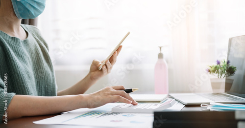 accounting  taxes and finances concept - woman with smartphone and calculator wearing face protective medical mask for protection from virus disease at home.